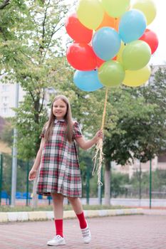 charming teenage girl in checkered brown dress with bunch of colorful balloons. school girl. pretty tween.