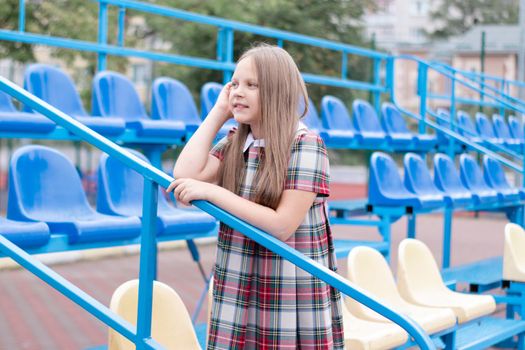 pretty girl in school dress uniform on the blue and yellow tribune of the school stadium. school time. tween