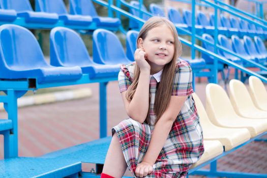 pretty girl in school dress uniform on the blue and yellow tribune of the school stadium. school time. tween