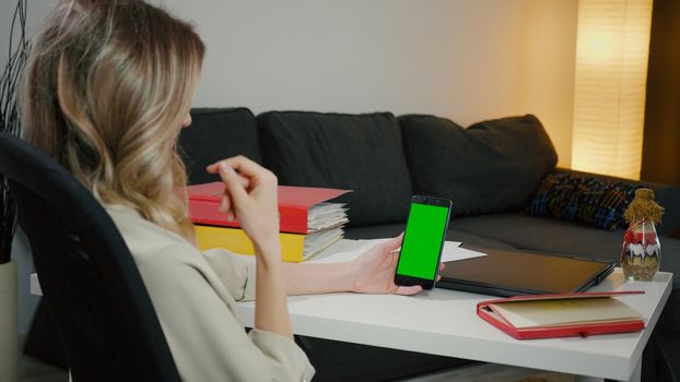 Back View of Woman at Phone with Green Screen for Copy Space. Chromakey Mockup. Talks on the phone, gesturing with hands. Business woman from home office has important phone video call.