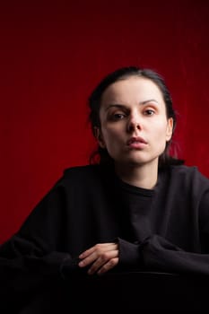 a woman in a black sweater sits at a chair, red background. High quality photo