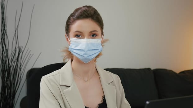 Close-up portrait of pretty woman with mask working on computer and then looking happy at camera. Blue eyes and blonde hair. Concept of working responsibly with mask and confident young woman.