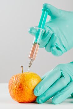 A hand in a medical glove inserts a syringe into apple. Harmful food additives. GMOs Concept. Injecting on apple at laboratory. Fruit genetic modification concept.