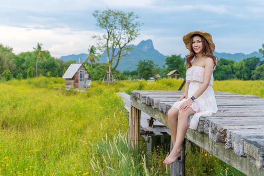 happy woman sitting on wooden bridge with yellow cosmos flower field