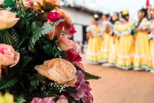Group of unrecognizable Nicaraguan folklore dancers on a stage with flowers in the foreground.