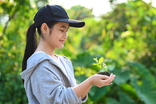 Adorable asian girl holding potted plant in hands against blurred green nature background. Saving the world, Earth day, Ecology concept.