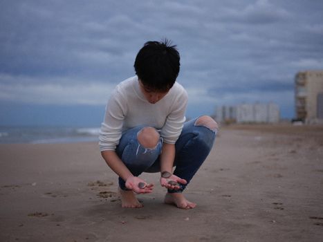 young girl squatting on the beach looking for shells in the sand, cloudy horizontal background