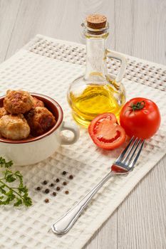 Fried meat cutlets in ceramic soup bowl, red tomatoes, glass bottle with sunflower oil, metal fork and black peppercorn on white kitchen towel