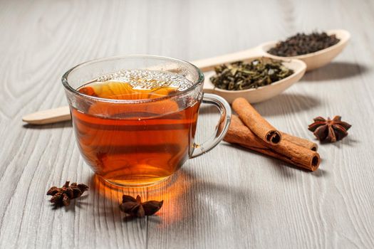 Cup of tea, two wooden spoons with leaves of green and black tea, cinnamon, star anise on grey boards