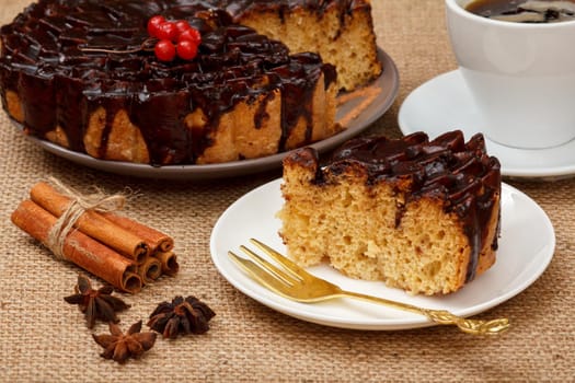 Sliced chocolate cake decorated with bunch of viburnum, cup of coffee, star anise and cinnamon on table with sackcloth