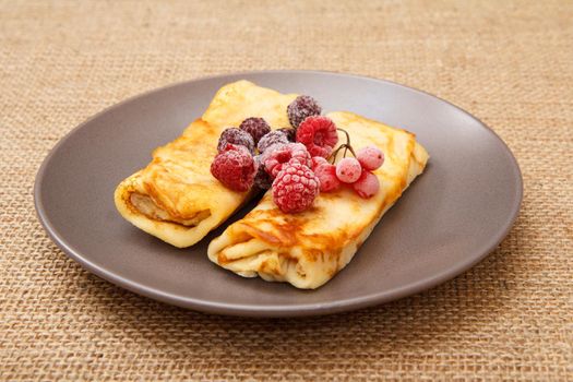 Homemade pancakes filled with cottage cheese and topped with frozen raspberries and blackberries on plate and sackcloth on background