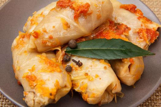 Delicious homemade cabbage rolls stuffed with rice and meat, topped by bay leaf, peppercorn and clove in plate on sackcloth