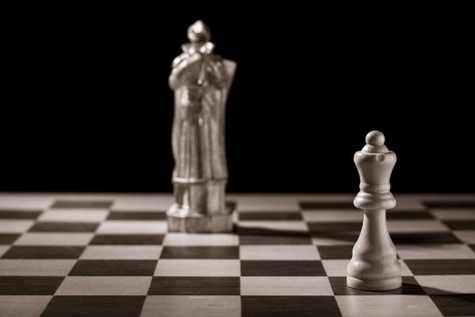 Classic white queen and the same chess piece in the form of medieval figure on the background. Selective focus on classic piece