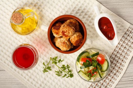 Fried meat cutlets in ceramic soup bowl, red tomatoes, white ceramic sauce boat with tomato sauce, glass of red wine, kitchen towel and glass bottle with sunflower oil on grey wooden boards. Top view