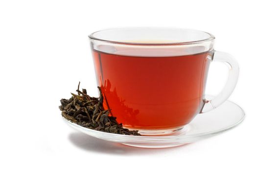 Glass cup of black tea on saucer with dry leaves of green tea on white isolated background