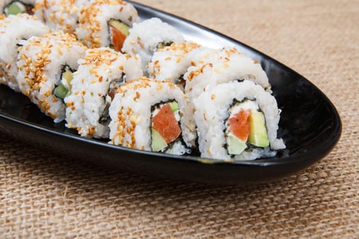 Uramaki sushi rolls with avocado and red fish on ceramic plate on sackcloth