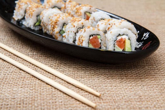 Uramaki sushi rolls with avocado and red fish on ceramic plate and wooden sticks on sackcloth