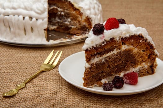 Sliced homemade biscuit cake decorated with whipped cream on table with sackcloth