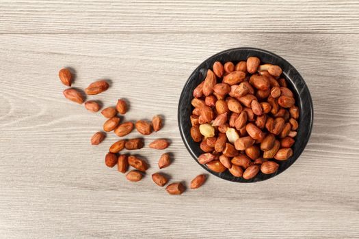 Top view of peanuts in black porcelain bowl and beside it on grey wooden background