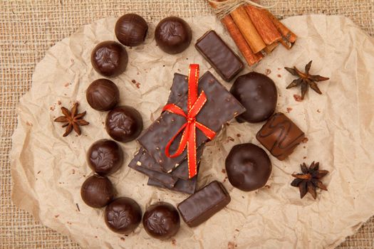 Chocolate candies various shape and chocolate bars with nuts put on piece of pack paper in the form of a heart with stars anise and cinnamon. Top view