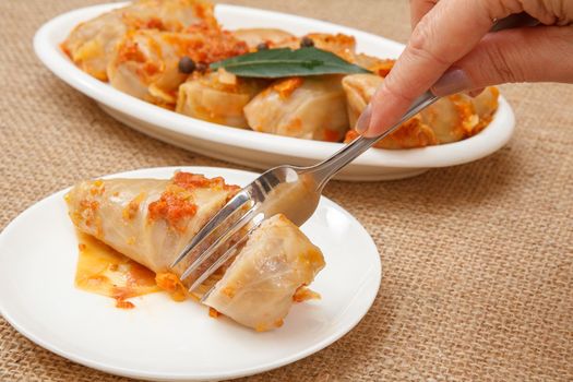 Female hand holding a fork and going to taste homemade cabbage rolls stuffed with rice and meat lying on white plate