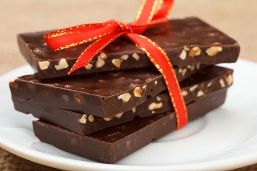 Chocolate bars with nuts tied with red ribbon on white saucer. Shallow depth of field