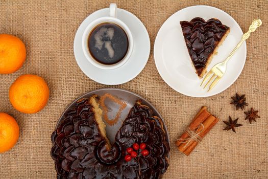 Sliced chocolate cake decorated with bunch of viburnum, cup of coffee, oranges, star anise and cinnamon on table with sackcloth. Top view