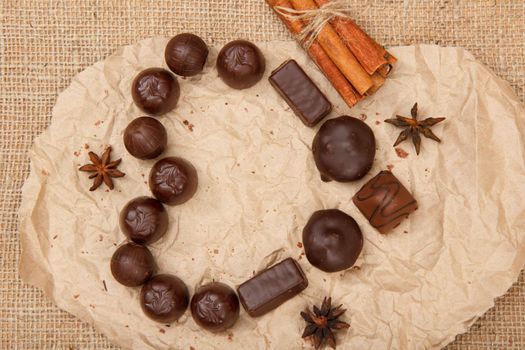 Chocolate candies rectangular and round shape put on pack paper in the form of a heart with stars anise and cinnamon. Top view