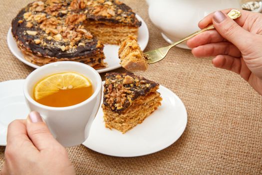 Female hands holding a cup of tea with slice of lemon and fork and going to taste homemade chocolate cake