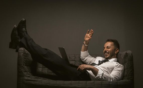 Businessman communicates using a laptop computer while lying on a sofa. Online business meeting. Work from home concept. Toned image.