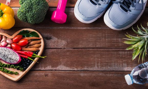 Top view of various fresh organic fruit and vegetable in heart plate and sports shoes, dumbbell and water, studio shot on wooden gym table, Healthy diet vegetarian food concept, World food day