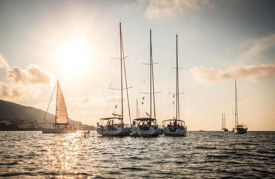 Picturesque seascape with sailboats, moored in calm rippled water, near hilly coast in sunset time with clouds on sky