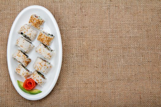 Uramaki sushi rolls with red fish and pickled ginger, piece of avocado on ceramic plate on sackcloth. Top view with copy space