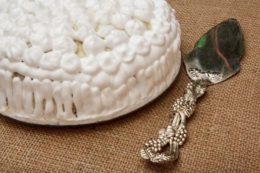 Biscuit cake decorated with whipped cream and silver cake lifter beside it on table with sackcloth