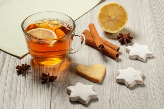 Cup of tea with slice of lemon, gingerbread cookies in star and heart shape, cinnamon and star anise on wooden boards
