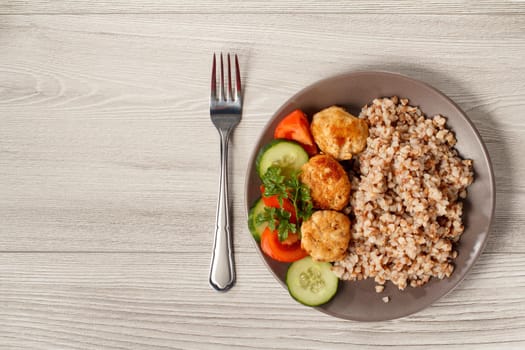 Plate with buckwheat, fried meat cutlets, pieces of fresh cucumbers and tomatoes decorated with branch of fresh parsley with knife fork. Top view