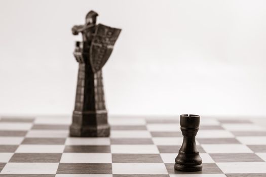 Classic black rook and the same piece in the form of medieval figure on the background. Selective focus on classic piece