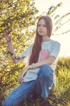 Portrait of a beautiful happy teenage girl outdoors in spring. A girl poses in a blooming spring garden.