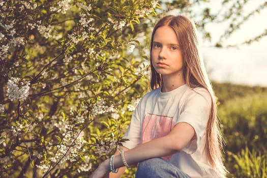 Portrait of a beautiful happy teenage girl outdoors in spring. A girl poses in a blooming spring garden.