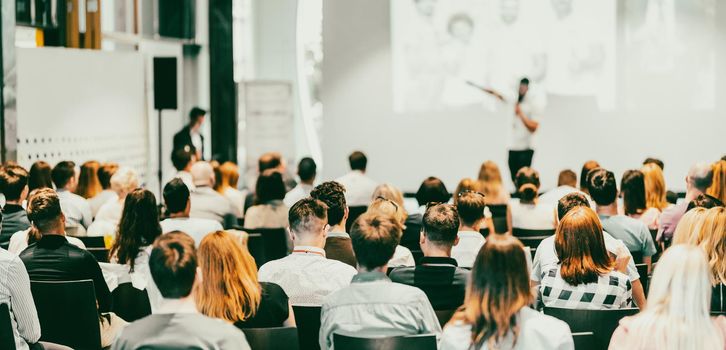 Speaker giving a talk in conference hall at business event. Rear view of unrecognizable people in audience at the conference hall. Business and entrepreneurship concept.