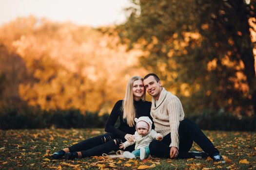 Portrait of attractive husband and blonde wife holding their surprised child. Handsome man helping pretty woman caring about little baby. Young happy family smiling at camera and standing together.