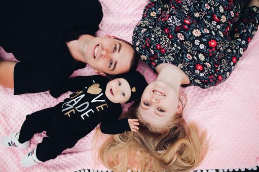 Close up from above of young happy family lying on ground outside. Attractive wife and husband with little baby looking at camera and smiling. Beautiful couple enjoying moment with their lovely child.