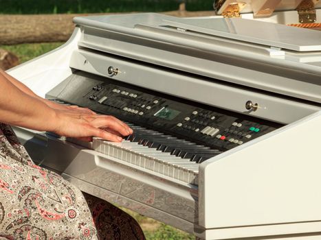 Lady hands playing white electric piano outdoors, keyboard with dust