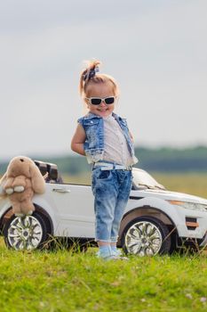 girl in sunglasses stands in front of a white children's car