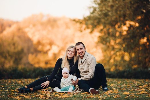 Portrait of attractive husband and blonde wife holding their surprised child. Handsome man helping pretty woman caring about little baby. Young happy family smiling at camera and standing together.