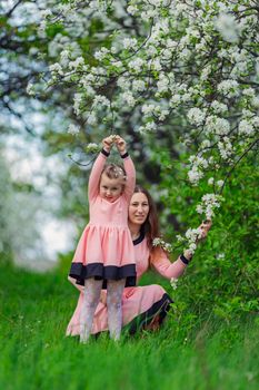 mother and daughter sit in the apple orchard in spring