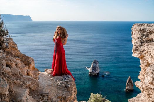 A woman in a flying red dress fluttering in the wind and a straw hat against the backdrop of the sea