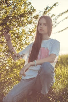 Portrait of a beautiful happy teenage girl outdoors in spring. A girl poses in a blooming spring garden.