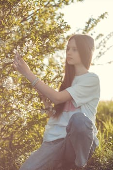 Portrait of a beautiful happy teenage girl outdoors in spring. A girl poses in a blooming spring garden.