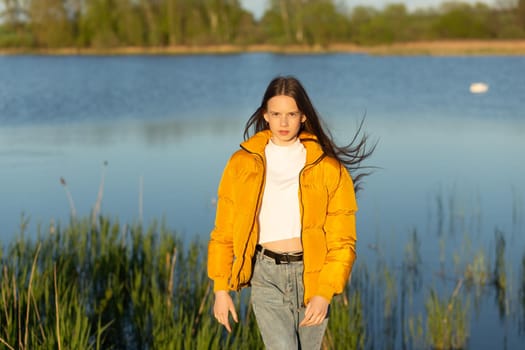 Portrait of stylish weared teenage girl outdoors in spring. A girl poses on lakes shore.